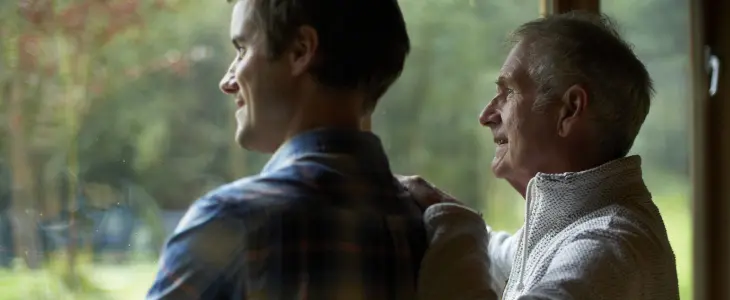 an elderly man and his sun staring out the window